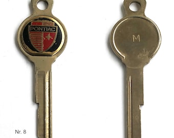 May include: Two gold-colored keys with a round head. One key has a black and gold emblem with the word "PONTIAC" in red letters. The other key has the letter "M" engraved on the head. Both keys have a number "8" printed on the bottom.