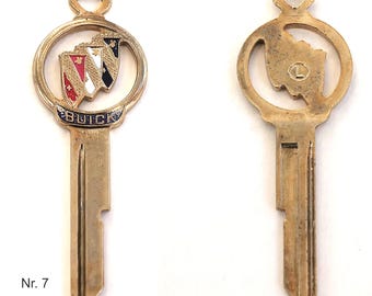 May include: A gold-coloured car key with a Buick logo on the top. The logo is a red, white and blue shield with a gold star on top. The key is labelled "Nr. 7".