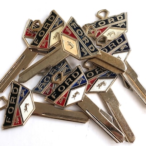 Könnte beinhalten: Eine Gruppe von Vintage-Ford-Autoschlüsseln mit goldfarbenen Metallschlüsselrohlingen und bunten Ford-Emblemen aus Emaille. Die Embleme zeigen ein stilisiertes Pferd und das Wort "FORD" in Schwarz, Rot, Blau und Weiß.