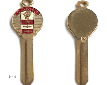 May include: A gold-toned metal key blank featuring a circular head with the text COMET in red enamel, a profile of a helmeted figure, and horizontal red and white stripes. The reverse side is plain gold-toned metal with a stamped letter K.