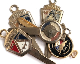 May include: Five vintage gold-toned keychains with the word "FORD" on each. The keychains feature different designs, including a shield with a blue, white, and red crest, a circular design with a red, white, and blue center, and a black and gold design with a stylized car.