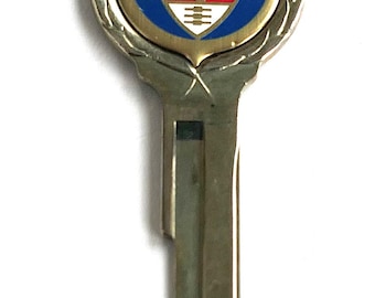 May include: A silver-toned metal key featuring a circular head with a decorative border. The centre displays a blue and red shield emblem with the word MERCURY printed in white text above a stylised profile of a Roman god figure.