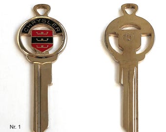 May include: A gold-colored car key with a Chrysler logo on one side and a steering wheel on the other. The key is labeled "Nr. 1".