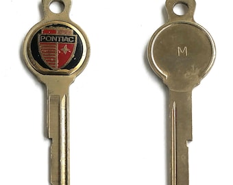 Può includere: Due chiavi in metallo color ottone. La chiave a sinistra presenta una testa circolare con uno stemma Pontiac nero, rosso e bianco. La chiave a destra ha una testa circolare liscia con la lettera M stampata al centro. Entrambe hanno lama standard.