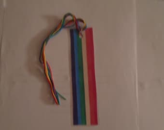 May include: A rainbow-coloured bookmark with a white string attached. The bookmark is made of clear plastic and has a rainbow design.