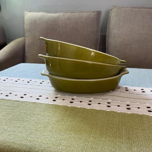May include: Three green ceramic ramekins stacked on top of each other on a green and white tablecloth.
