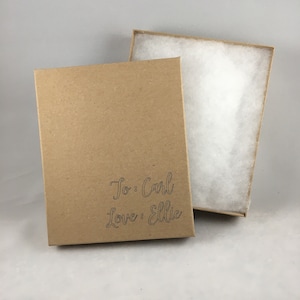 May include: A brown cardboard gift box with a white tissue paper lining. The box has a personalized message that reads "To: Carl Love: Ellie".