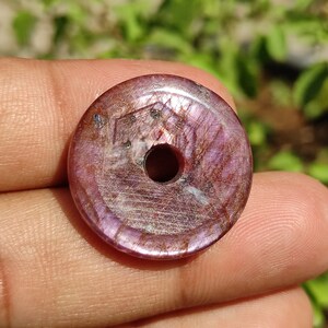 May include: A round, flat, purple and silver gemstone bead with a hole in the centre. The bead has a smooth, polished surface and a slightly iridescent sheen.