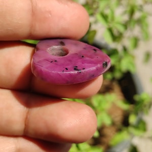 May include: A heart-shaped pink gemstone pendant with black flecks. The pendant has a hole drilled through the top for stringing.