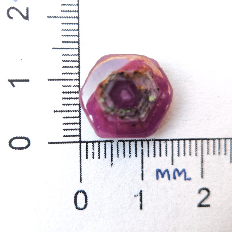 May include: A pink gemstone with a hexagonal pattern inside. The gemstone is about 1 cm in diameter.