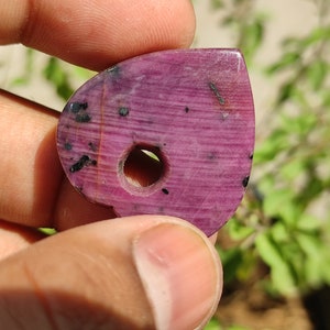 May include: A pink and black heart-shaped gemstone pendant with a hole drilled through the centre. The gemstone has a striated pattern and black inclusions.