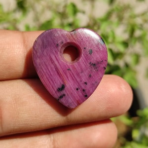 May include: A pink heart-shaped pendant with a hole in the centre. The pendant is made of polished stone with black flecks throughout.