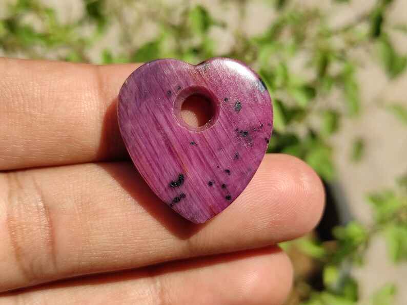 May include: A pink heart-shaped pendant with a hole in the centre. The pendant is made of polished stone with black flecks throughout.