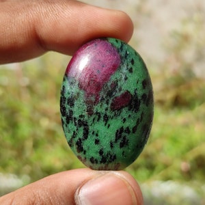 May include: Oval-shaped green and pink gemstone cabochon with black flecks.