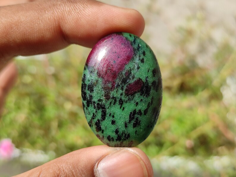 May include: Oval-shaped green and pink gemstone cabochon with black flecks.