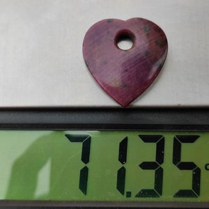 May include: A heart-shaped pink gemstone with a hole drilled through the top, weighing 7.135 carats.