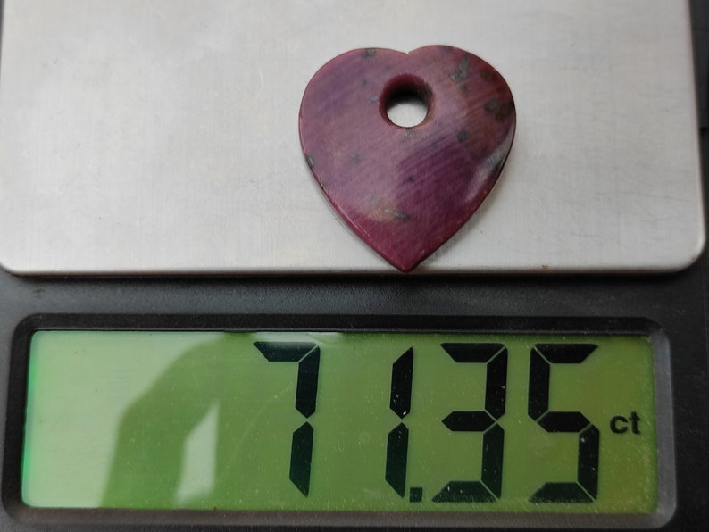 May include: A heart-shaped pink gemstone with a hole drilled through the top, weighing 7.135 carats.