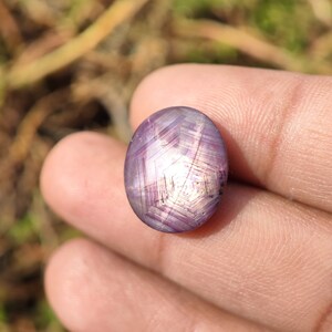 May include: A purple star ruby gemstone with a star-shaped pattern in the center. The gemstone is oval-shaped and has a smooth, polished surface.