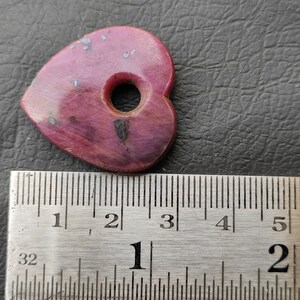 May include: A pink heart-shaped guitar pick with a hole in the centre. The pick is approximately 2.5 cm wide and 3.8 cm long.