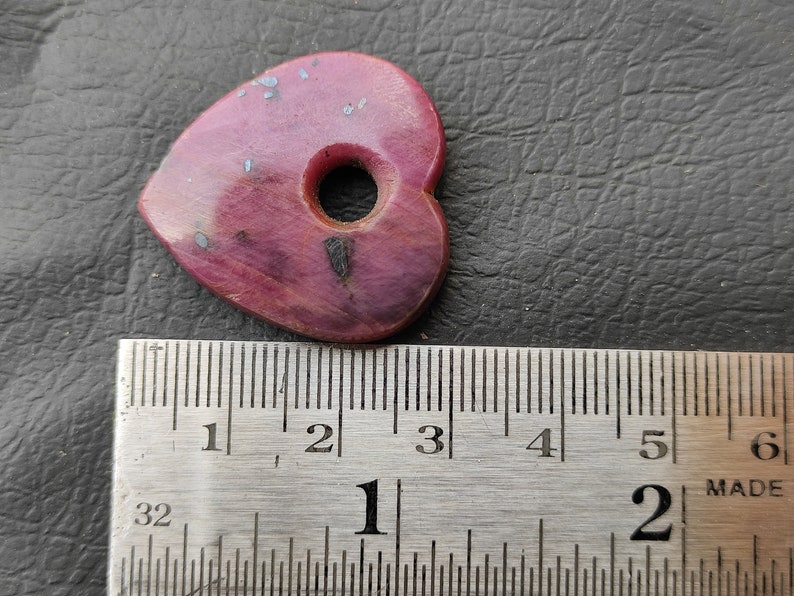 May include: A pink heart-shaped guitar pick with a hole in the centre. The pick is approximately 2.5 cm wide and 3.8 cm long.