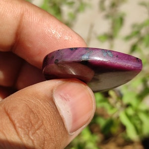May include: A close-up of a purple and black gemstone cabochon. The gemstone is smooth and polished, with a heart shape.