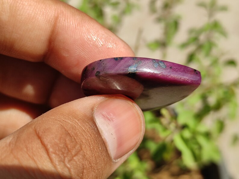 May include: A close-up of a purple and black gemstone cabochon. The gemstone is smooth and polished, with a heart shape.