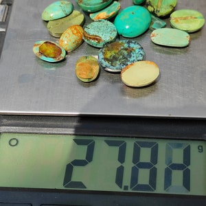 May include: A collection of 17 turquoise cabochons of various sizes and shades of green and blue, weighing 27.84 grams, on a digital scale.