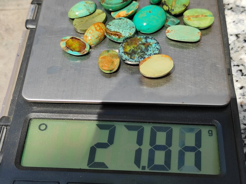May include: A collection of 17 turquoise cabochons of various sizes and shades of green and blue, weighing 27.84 grams, on a digital scale.