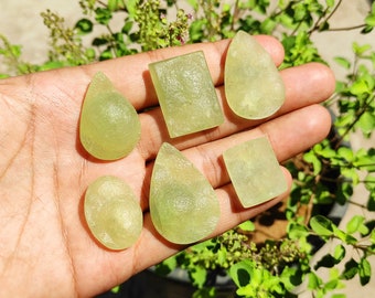 May include: Five green gemstone cabochons in various shapes, including teardrop, oval, and square, displayed on a hand.