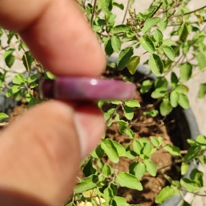 May include: A close-up of a purple and white ring held between two fingers. The ring is made of a smooth, shiny material.