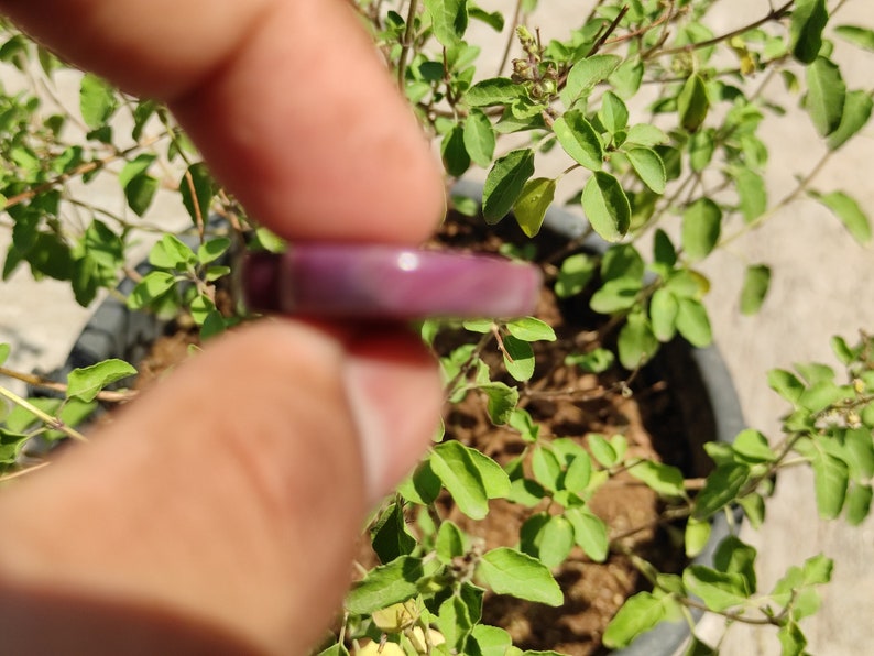 May include: A close-up of a purple and white ring held between two fingers. The ring is made of a smooth, shiny material.