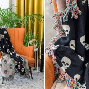 May include: A black and white throw blanket with a skull pattern. The blanket has a colourful fringe border and is draped over an orange armchair.