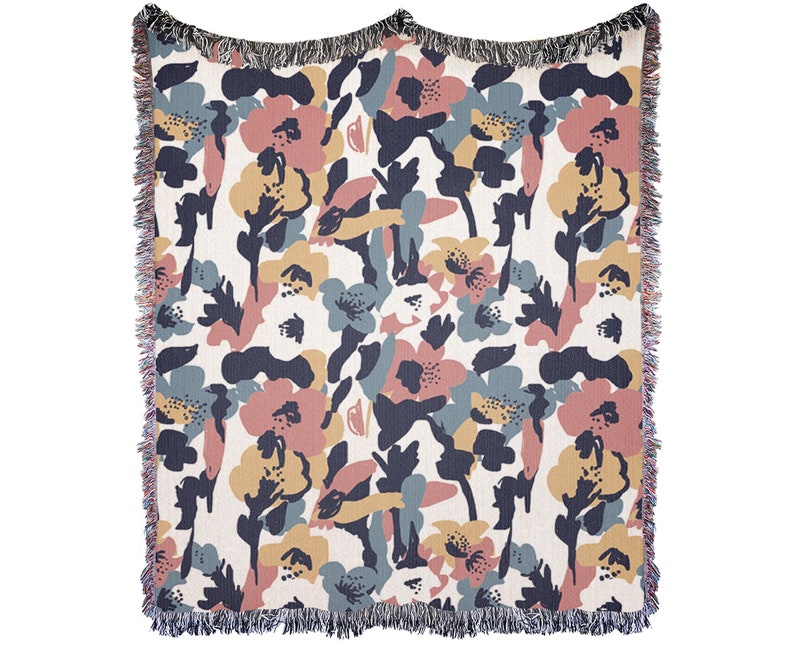 May include: A woven throw blanket with a floral pattern. The design features abstract flowers in shades of pink, blue, and yellow on a cream background. The blanket has a fringed edge and is suitable for home decor.