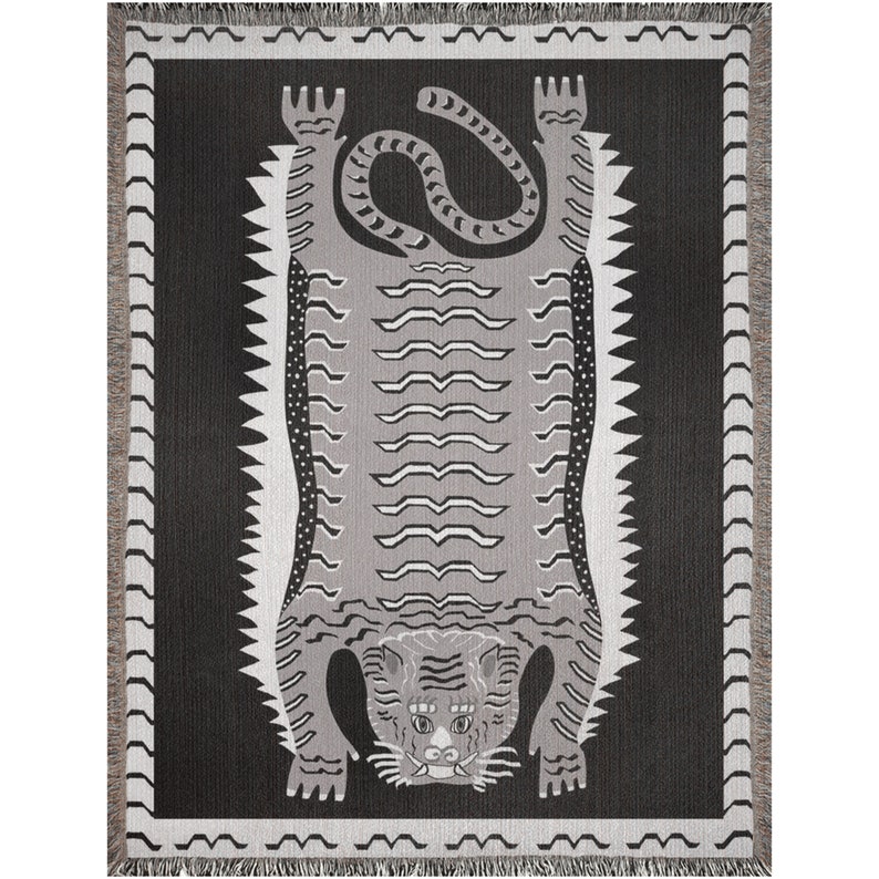 May include: A black and white woven tapestry featuring a stylized tiger design. The tiger is depicted upside down with its paws in the air and its tail curled around its body. The background is a solid black color.