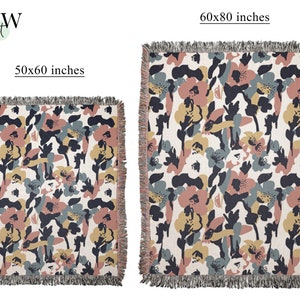 May include: Two floral-patterned throw blankets. The smaller blanket is 50x60 inches, and the larger is 60x80 inches. The design features abstract flowers in muted colors of pink, navy, yellow, and gray on a cream background. Both blankets have fringed edges.