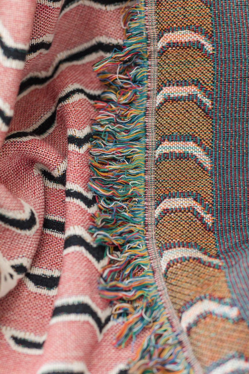 May include: A pink and black striped woven throw blanket with a fringe border. The fringe is made of multi-colored yarn.
