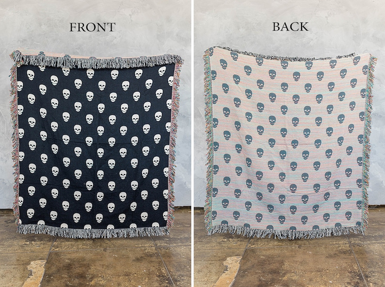 May include: A black and white woven throw blanket with a skull pattern on the front and a pink and blue striped pattern with a skull pattern on the back. The blanket has fringe on all sides.