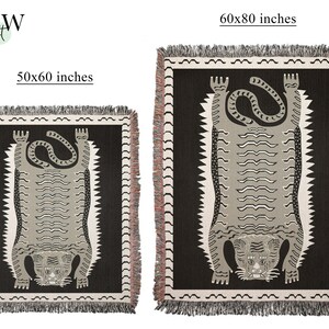 May include: Two woven tapestry throw blankets featuring a black and white tiger design. The smaller blanket is 50x60 inches and the larger blanket is 60x80 inches.