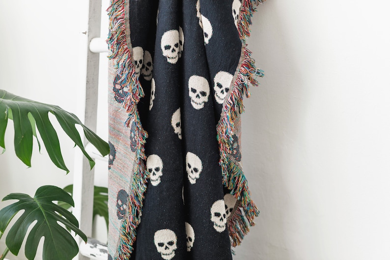 May include: Black throw blanket with a white skull pattern and fringe trim.