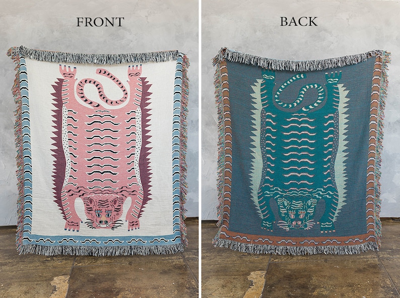 May include: A woven tapestry throw blanket features a pink and teal tiger design. The front of the blanket features a pink tiger with black stripes, while the back features a teal tiger with black stripes. The blanket has a fringe border.