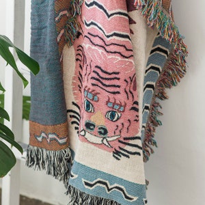 May include: A pink and blue woven throw blanket with a tiger face design. The blanket has fringe on all sides.