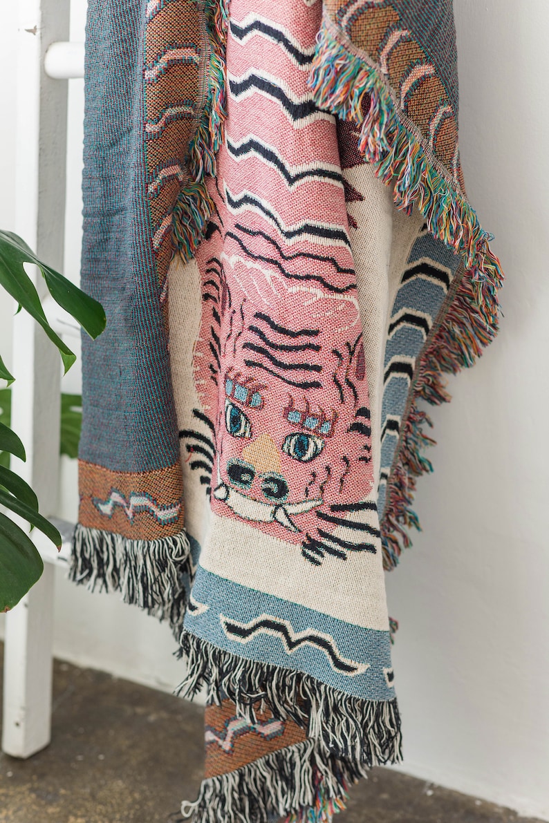May include: A pink and blue woven throw blanket with a tiger face design. The blanket has fringe on all sides.