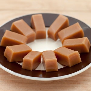 May include: A plate of caramel sweets arranged in a circle on a brown surface. The sweets are a light brown colour and have a smooth, glossy finish.