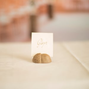 May include: A small, brown, acorn-shaped place card holder with a white card that says "Glyn" in gold lettering.