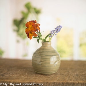 Peut inclure: Un petit vase rond en céramique gris avec une surface texturée contient un bouquet de fleurs orange et violettes.