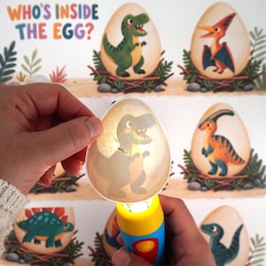 May include: A handheld flashlight toy with a yellow and blue handle, projecting a light through a translucent egg-shaped card featuring a green dinosaur illustration. The background displays a poster titled Who's Inside The Egg? with various dinosaur eggs.