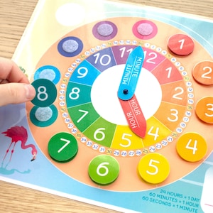 May include: A colorful clock face with numbers 1 through 12, and a separate minute hand and hour hand. The clock face is divided into 60 sections, with each section representing one minute. The clock face is surrounded by a ring of numbers 1 through 12, with each number representing one hour. The clock face is also surrounded by a ring of numbers 1 through 60, with each number representing one minute. The clock face is made of cardboard and has a bright, colorful design. The clock face is a teaching tool for learning about time.