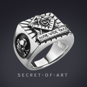 May include: A silver ring with a skull and crossbones on one side and a Masonic symbol with the inscription "Aude Vide Tace" on the other side.