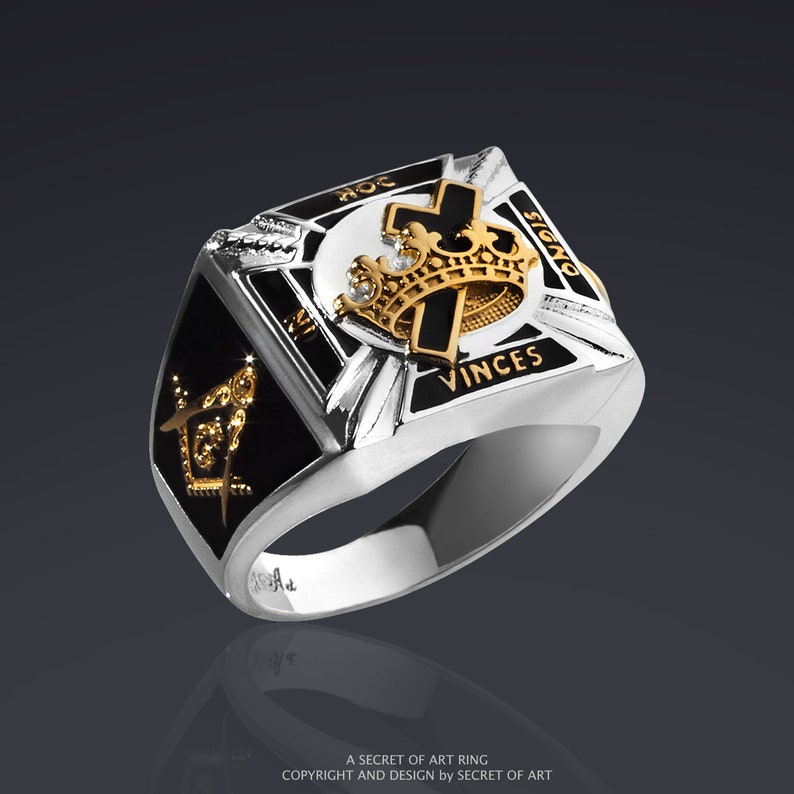 May include: A silver ring with a black enamel design featuring a crown, cross, and the words "VINCES" and "SIGNO".