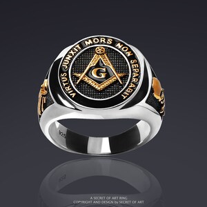 May include: A silver ring with a black enamel center featuring a gold Masonic compass and square with the letter 'G' inside. The ring has the inscription 'Virtus Junxit Mors Non Separabit' around the edge.